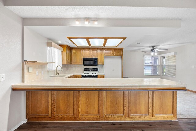 1086 Hickory Ave, Tehachapi, CA 93561 - kitchen with a sink, white range with gas stovetop, brown cabinets, black microwave, and a peninsula