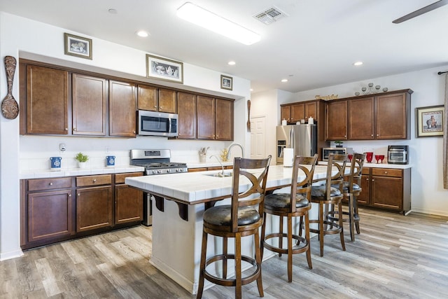 1413 La Quinta Way, Madera, CA 93638 - kitchen featuring appliances with stainless steel finishes, tile counters, light wood finished floors, a kitchen bar, and recessed lighting