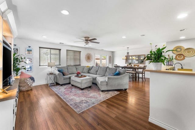 living room featuring dark wood-type flooring, ceiling fan with notable chandelier, and sink