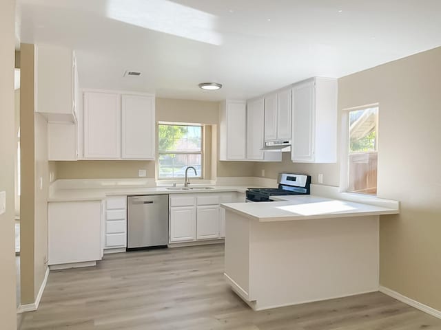 kitchen featuring kitchen peninsula, stainless steel dishwasher, sink, white range with gas stovetop, and white cabinetry