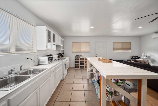 kitchen with white appliances, light tile patterned floors, a sink, white cabinets, and a wall mounted air conditioner