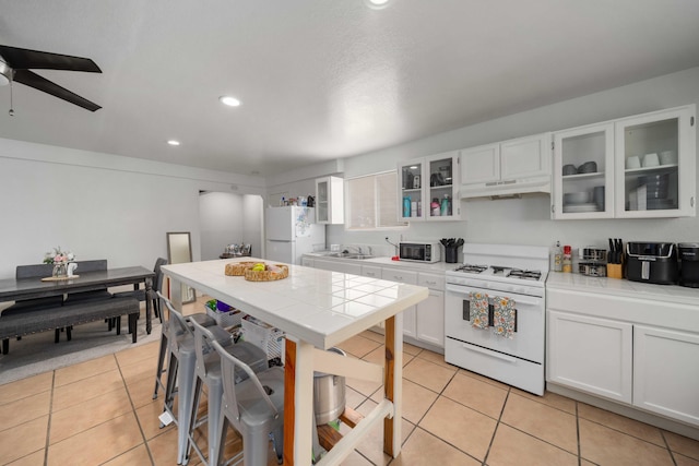 kitchen featuring under cabinet range hood, white appliances, tile counters, and light tile patterned floors