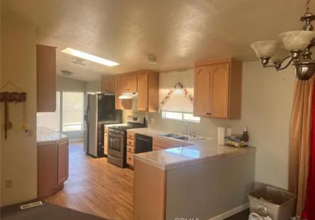 kitchen with sink, kitchen peninsula, a chandelier, light brown cabinetry, and appliances with stainless steel finishes