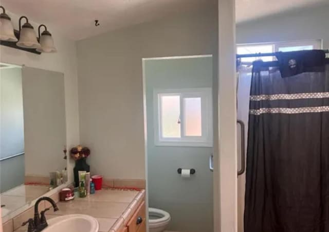 bathroom featuring vanity, a healthy amount of sunlight, vaulted ceiling, and toilet