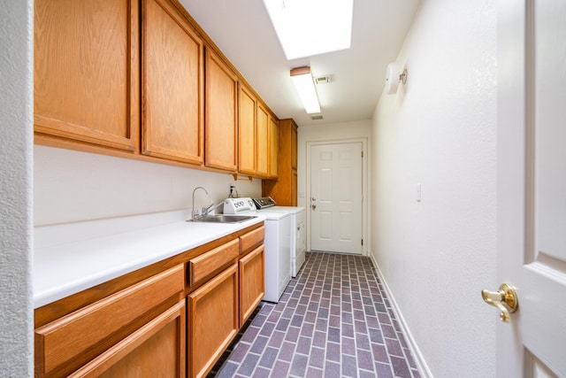 laundry room with brick floor, cabinet space, a sink, washer and dryer, and baseboards