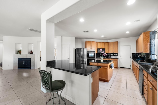 kitchen featuring sink, a kitchen breakfast bar, a center island, light tile patterned floors, and black appliances