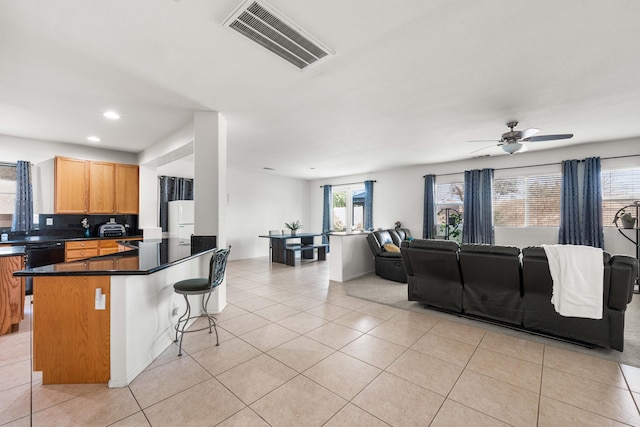 kitchen with light tile patterned flooring, dishwasher, ceiling fan, and a kitchen bar