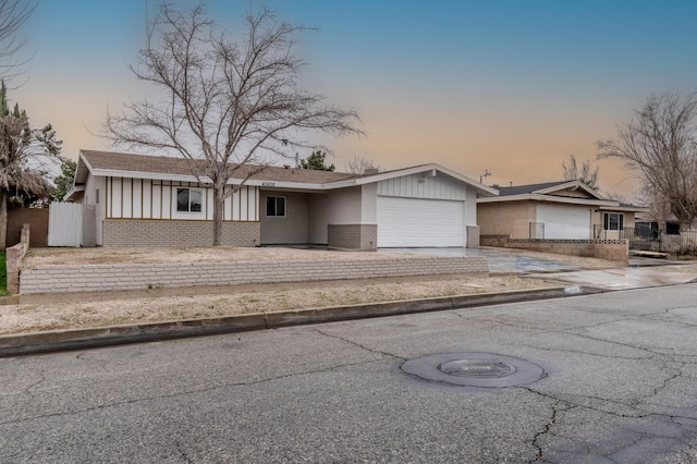 view of front facade with an attached garage, fence, concrete driveway, and brick siding