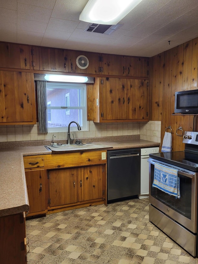 kitchen with sink, wood walls, and appliances with stainless steel finishes