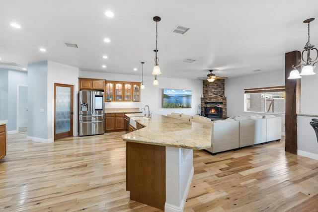 kitchen with light hardwood / wood-style floors, a kitchen island with sink, stainless steel refrigerator with ice dispenser, and hanging light fixtures