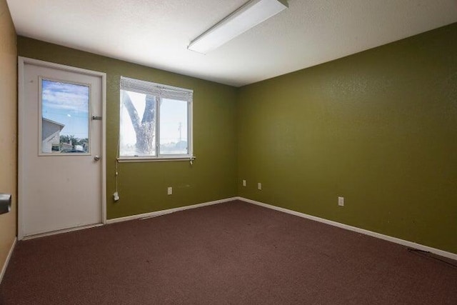 spare room featuring baseboards and dark colored carpet