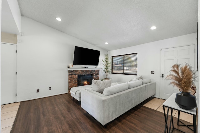 living room with lofted ceiling, a fireplace, hardwood / wood-style floors, and a textured ceiling