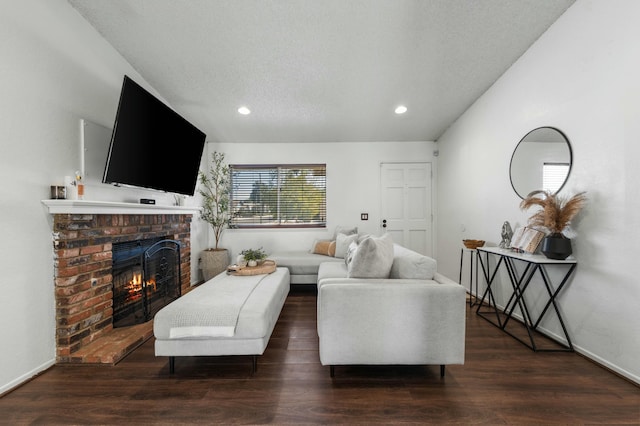 living room featuring lofted ceiling, dark hardwood / wood-style floors, a brick fireplace, and a textured ceiling