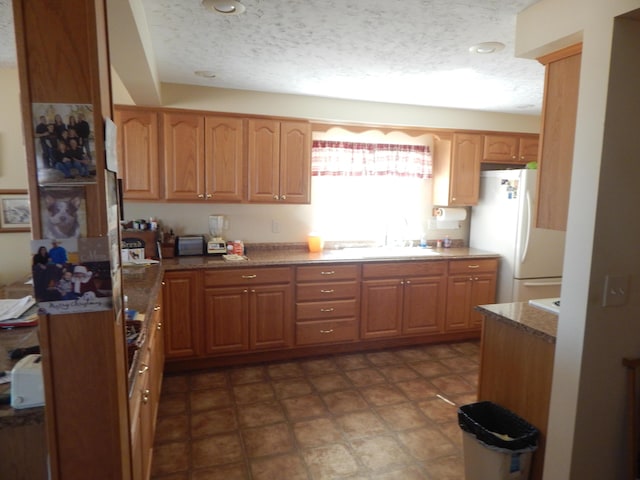 kitchen with stone counters, a textured ceiling, white fridge, and sink