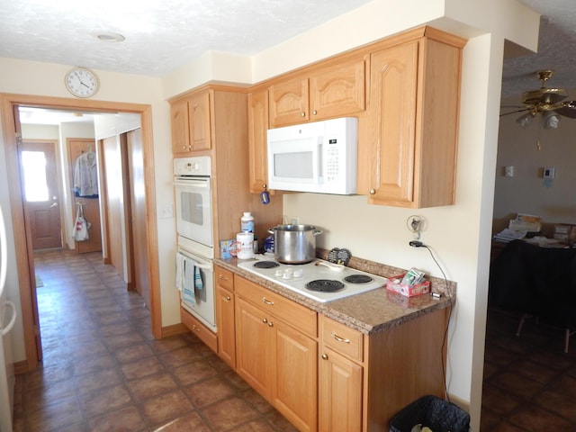 kitchen with light stone counters, white appliances, a textured ceiling, ceiling fan, and light brown cabinets