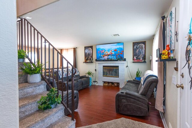 living room featuring wood finished floors, a glass covered fireplace, stairway, and visible vents