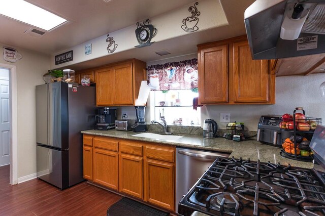 kitchen featuring range hood, a sink, freestanding refrigerator, dishwashing machine, and brown cabinetry
