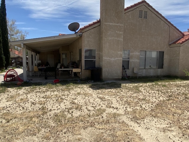 back of house featuring a tile roof, a chimney, a patio area, and stucco siding