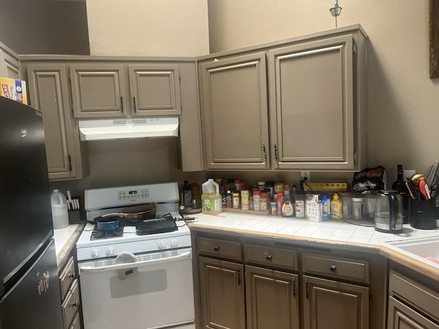 kitchen with under cabinet range hood, white gas range, freestanding refrigerator, tile countertops, and a textured wall