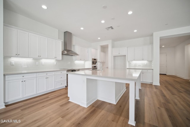 3716 Eliopulos Ranch Dr, Palmdale, CA 93551 - kitchen with wall chimney exhaust hood, a spacious island, tasteful backsplash, white cabinetry, and light wood-style flooring
