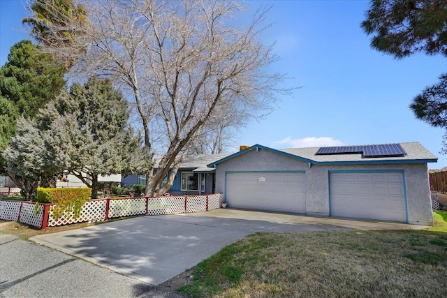 view of front of home featuring fence, roof mounted solar panels, stucco siding, driveway, and an attached garage