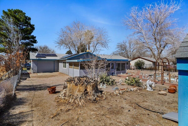 rear view of house with fence, roof mounted solar panels, a garage, a sunroom, and driveway