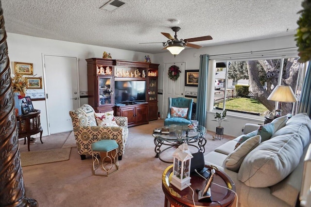 living area featuring visible vents, light carpet, a textured ceiling, and a ceiling fan