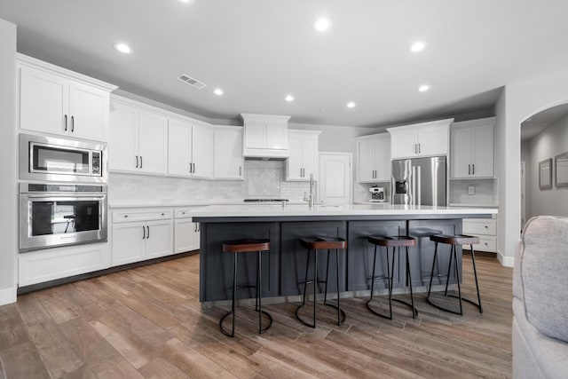 kitchen featuring a breakfast bar, sink, white cabinets, stainless steel appliances, and a center island with sink