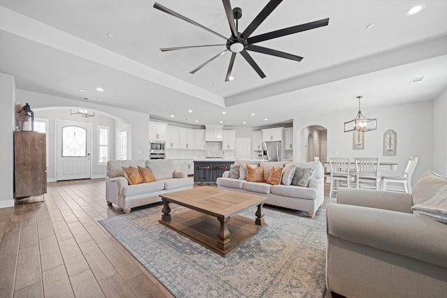 living room with ceiling fan with notable chandelier, hardwood / wood-style floors, and a tray ceiling