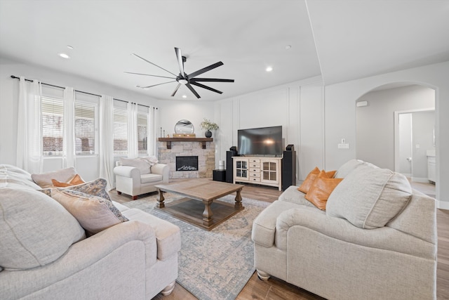 living room featuring hardwood / wood-style flooring, a stone fireplace, and ceiling fan