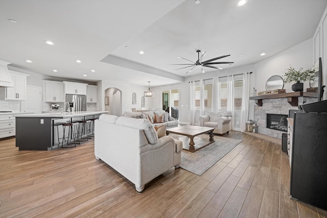 living room with ceiling fan, a stone fireplace, sink, and light hardwood / wood-style flooring