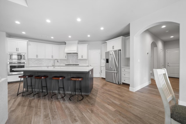 kitchen featuring white cabinetry, an island with sink, custom range hood, stainless steel appliances, and backsplash