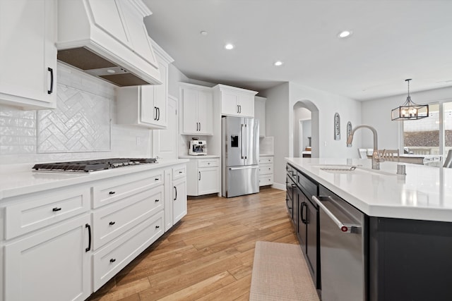 kitchen featuring sink, white cabinetry, decorative light fixtures, appliances with stainless steel finishes, and custom range hood