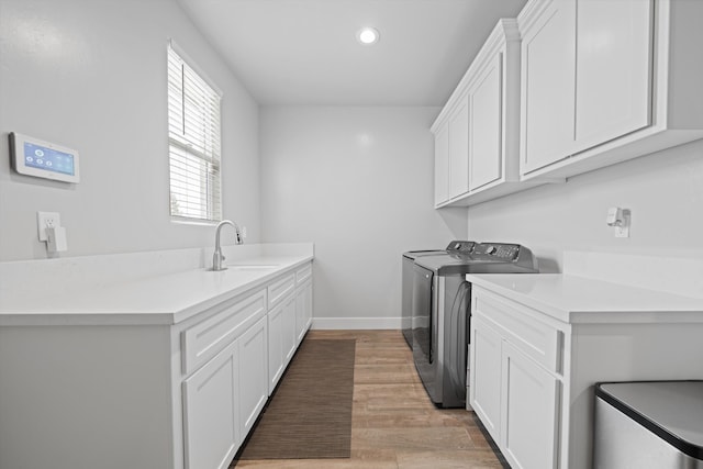 clothes washing area with sink, washing machine and dryer, cabinets, and light wood-type flooring