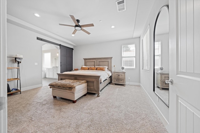 bedroom with connected bathroom, light colored carpet, a barn door, and ceiling fan