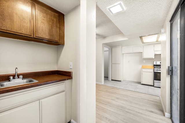 kitchen with sink, white cabinetry, a textured ceiling, stainless steel range with gas cooktop, and light wood-type flooring