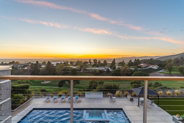 pool at dusk featuring a mountain view, a patio area, and a hot tub