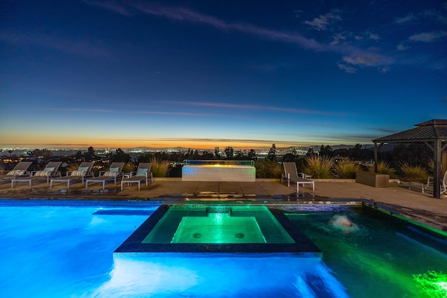 pool at dusk featuring an in ground hot tub, a gazebo, and a patio