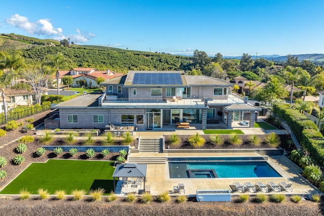 rear view of property featuring a swimming pool with hot tub, a balcony, and a patio