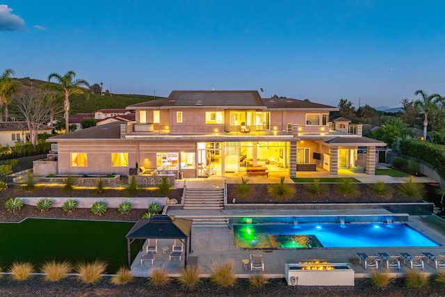 back house at dusk with outdoor lounge area, a patio, a balcony, and a pool with hot tub