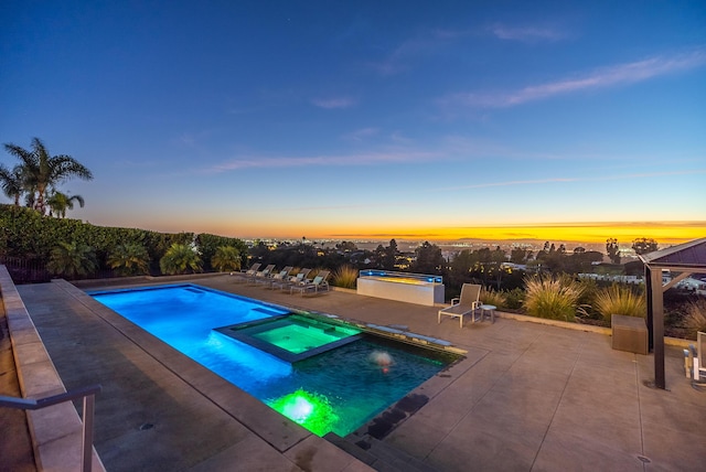 pool at dusk with a patio area and an in ground hot tub