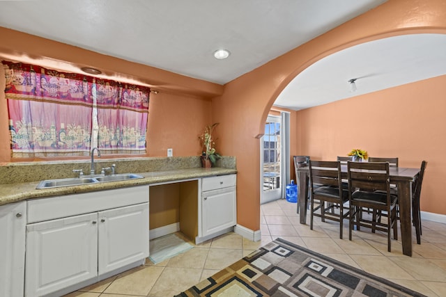 kitchen with arched walkways, light countertops, white cabinetry, a sink, and light tile patterned flooring