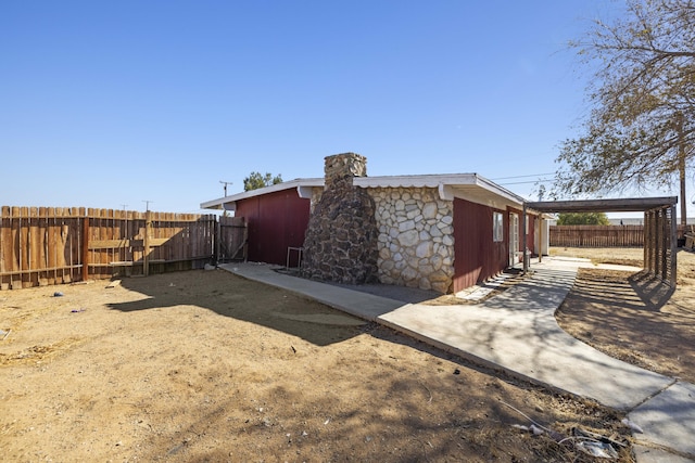 view of home's exterior featuring stone siding, a chimney, and fence