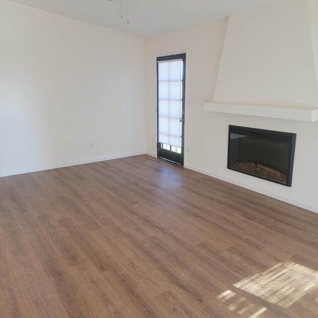 unfurnished living room with a large fireplace, baseboards, ceiling fan, and wood finished floors