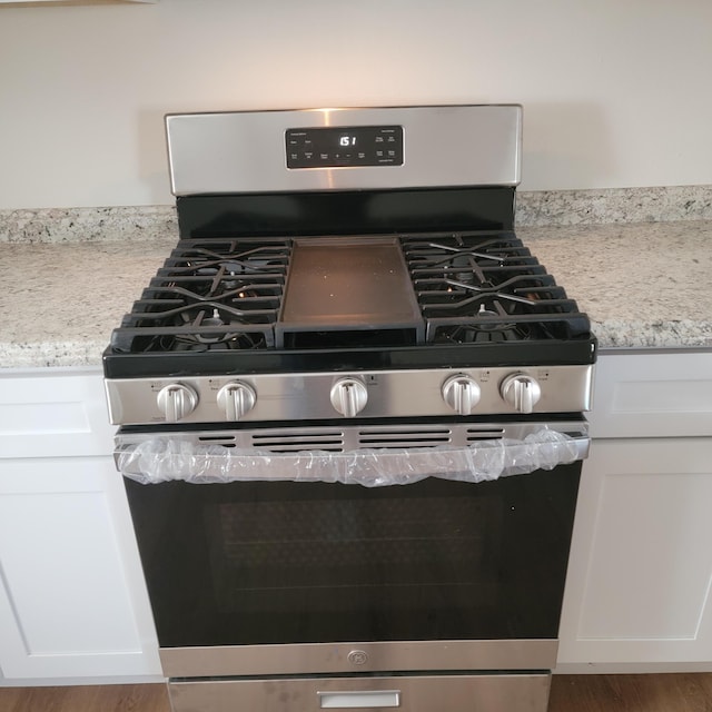 room details featuring white cabinets, light stone countertops, and gas range