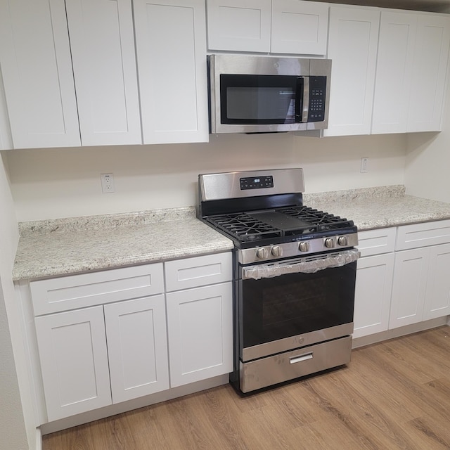 kitchen with white cabinets, appliances with stainless steel finishes, light wood-style floors, and light stone counters
