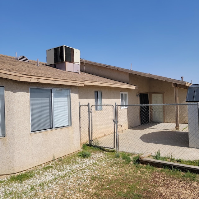 rear view of house with stucco siding, a gate, fence, and cooling unit