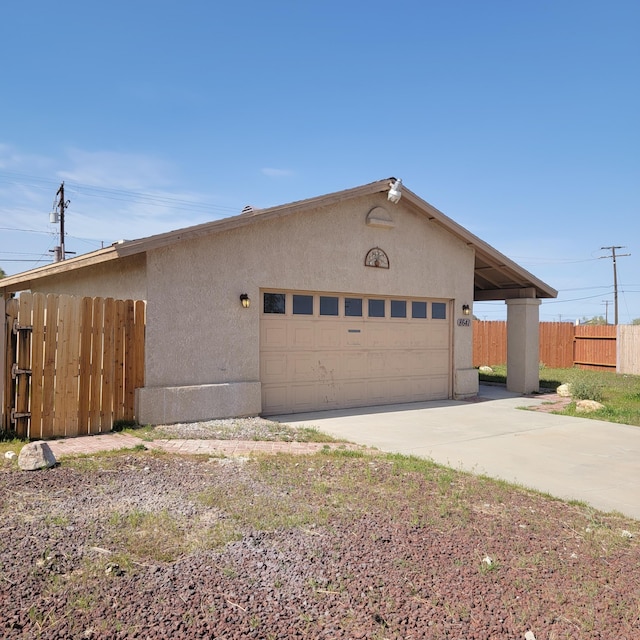 exterior space featuring stucco siding, an attached garage, fence, and concrete driveway