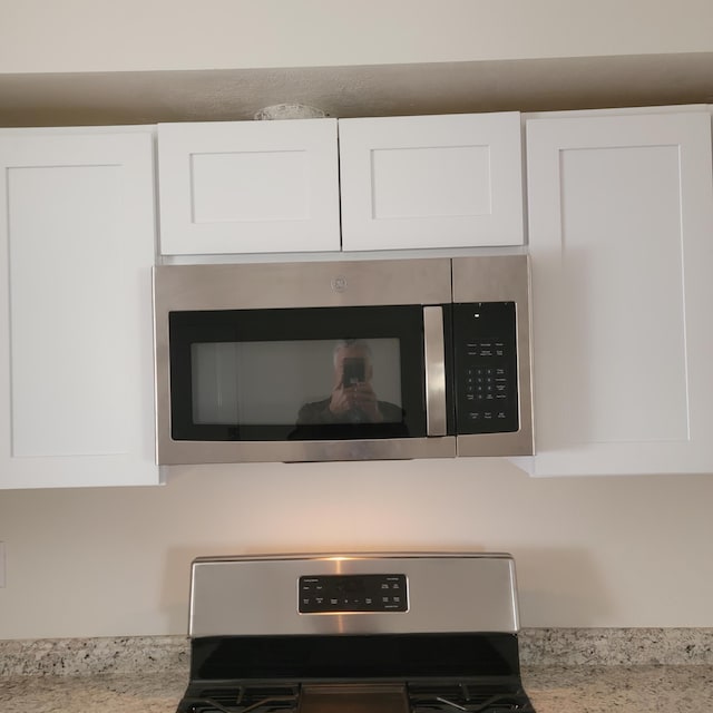 interior details with white cabinetry, range, and stainless steel microwave