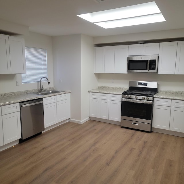 kitchen featuring light countertops, light wood-style flooring, stainless steel appliances, a sink, and white cabinets